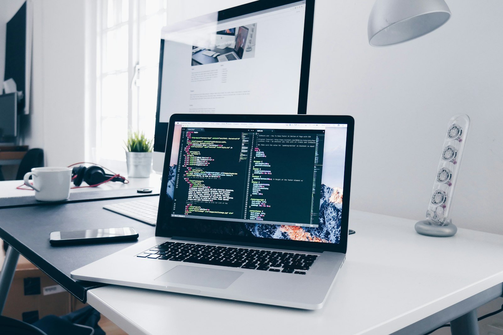 Laptop showing code next to a monitor displaying a website design, representing accessible website design work for NZ small business