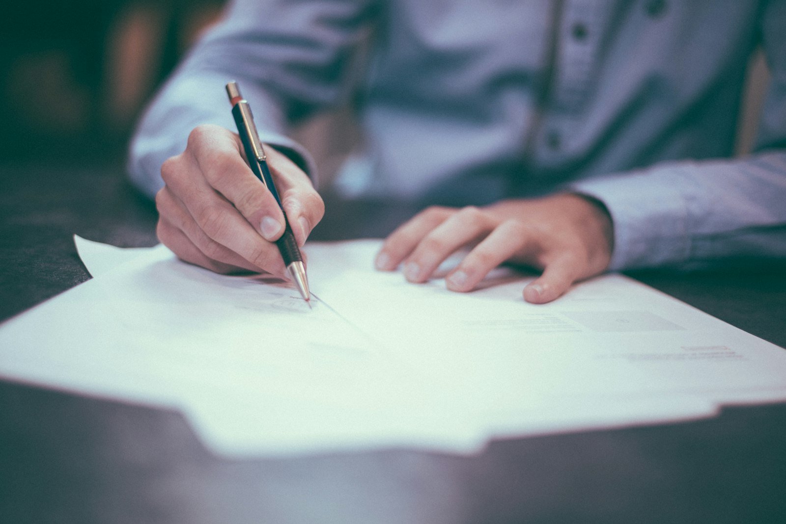 Person signing a business contract, representing website ownership and agency agreements for NZ small businesses
