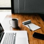 Laptop, coffee and a handwritten notepad on a desk, representing drafting website copy for a small business