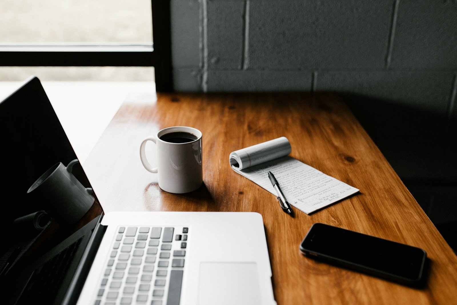 Laptop, coffee and a handwritten notepad on a desk, representing drafting website copy for a small business
