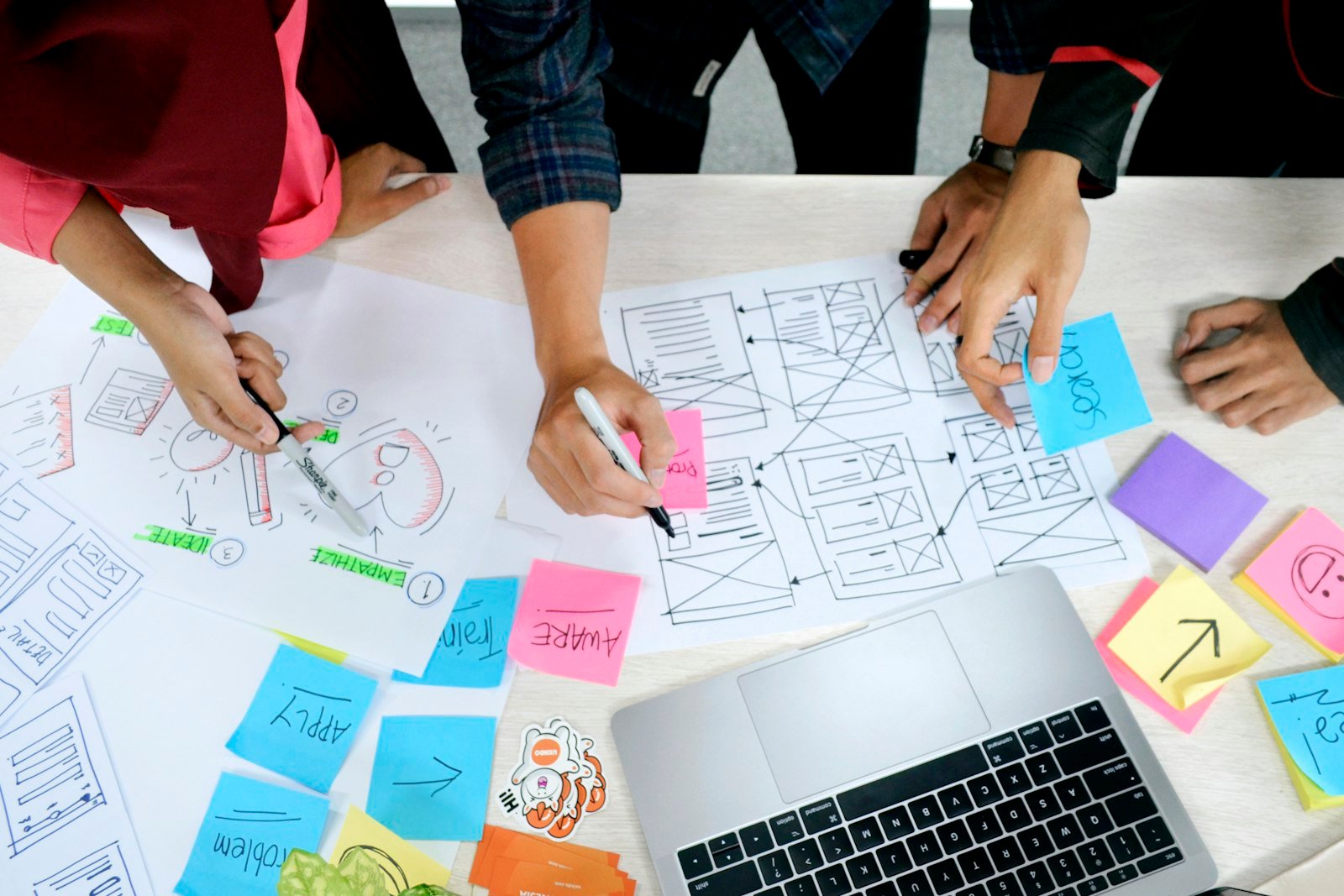 Design team sketching a website redesign sitemap and wireframe on paper next to a laptop