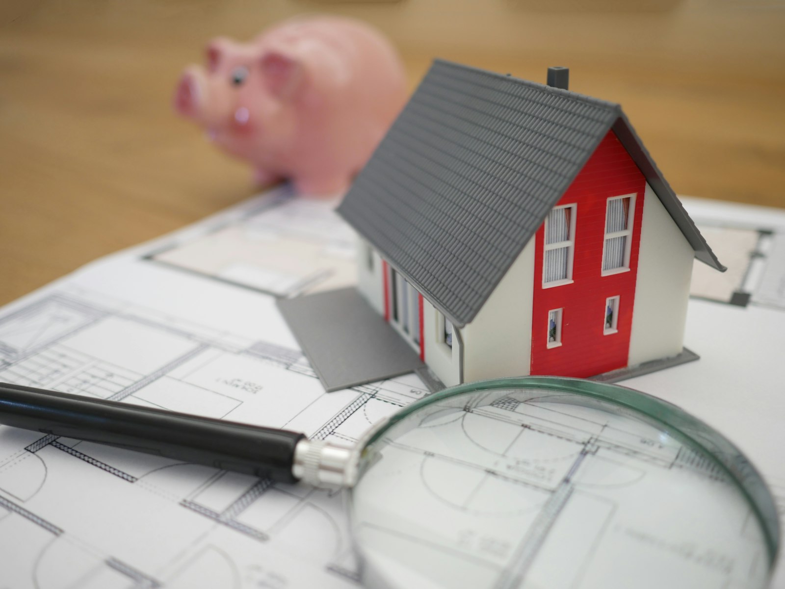 Toy house model with blueprint, pen and magnifying glass representing mortgage and home loan planning