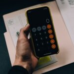 Hand holding a phone calculator over paperwork while comparing website design quotes